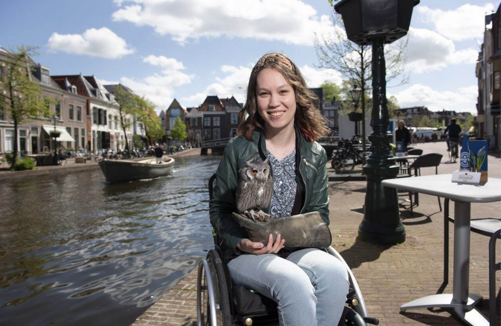 Jiska Ogier zit op een kade. Achter haar vaart een boot en staan huizen. Met een leren handschoen aan haar rechterhand houdt ze een uil vast.